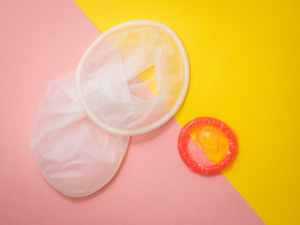A female condom next to a red male condom.