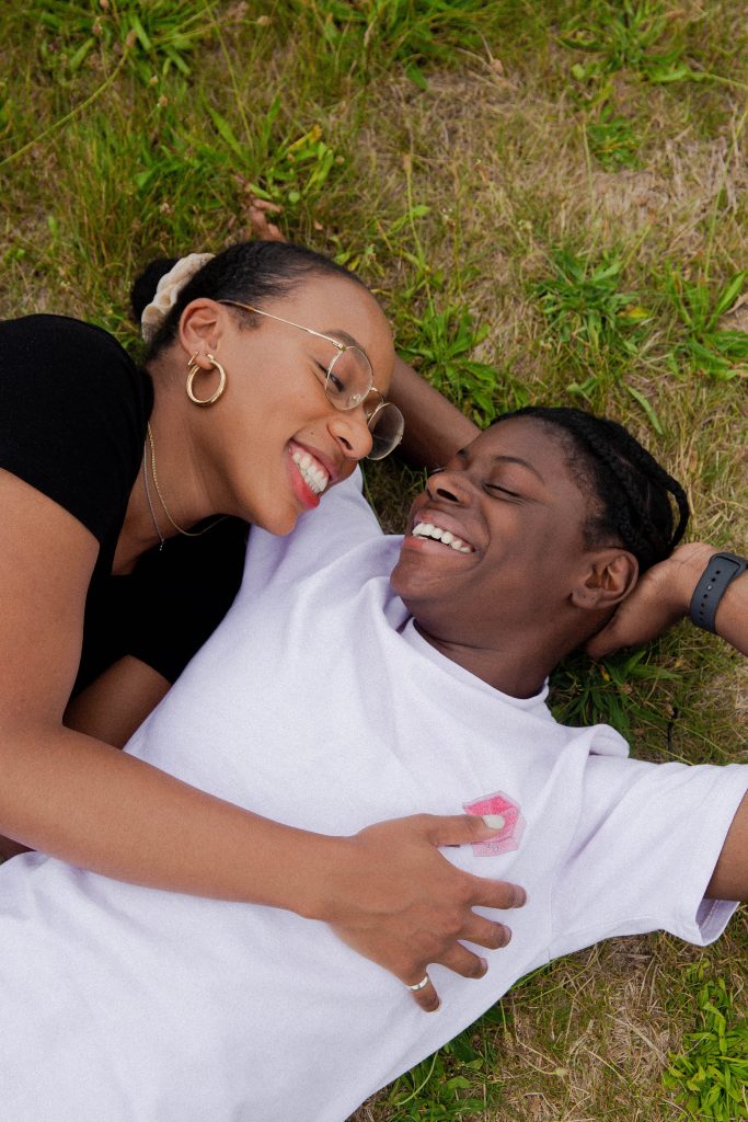 A couple lying on grass and smiling at each other.