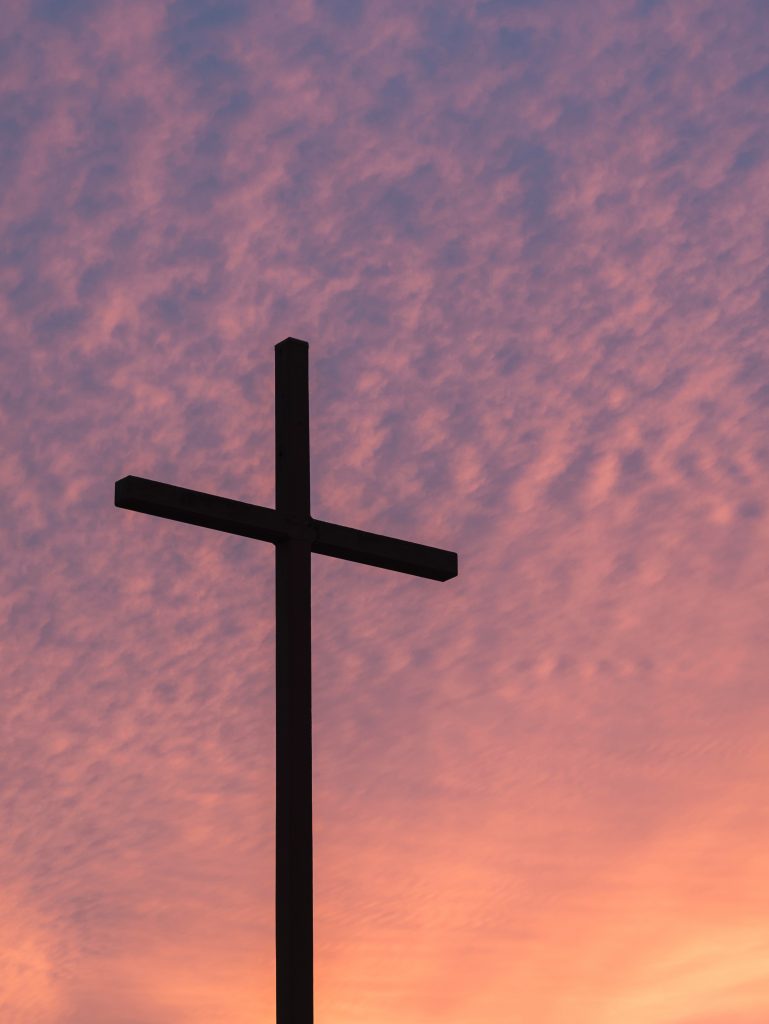 silhouette of a cross against a cloudy, pink sky.