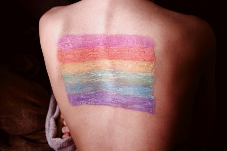 A person's naked back with a pride flag painted on it