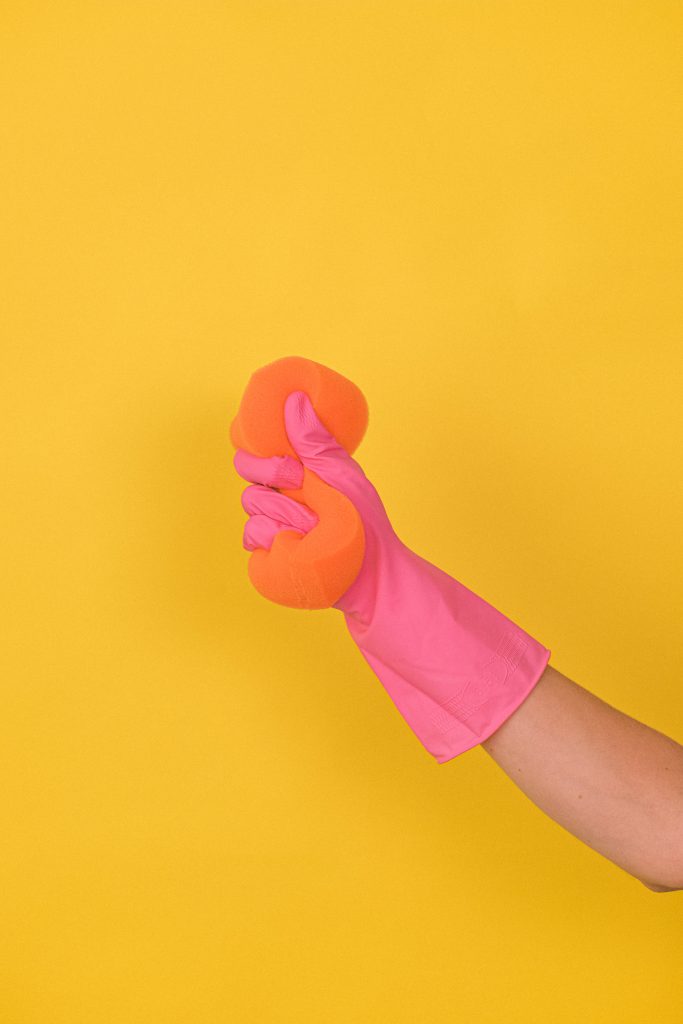 A person wearing a pink glove and squeezing an orange sponge.