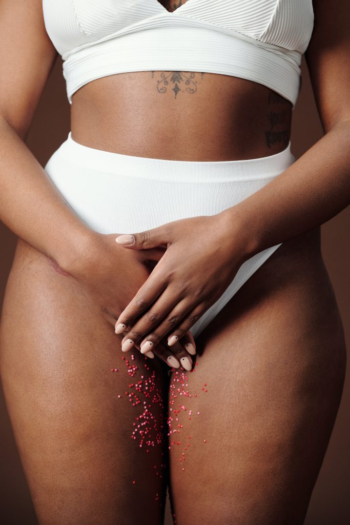 A person wearing a white bikini, with their hands covering their vulva area. There are red sparkles down the person's thighs.