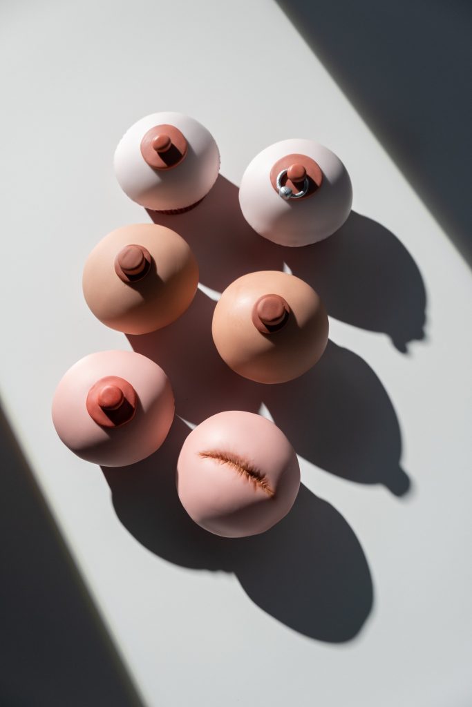 Three sets of breasts made from clay.  One set of breasts has a nipple piercing and another set has one breast without a nipple.