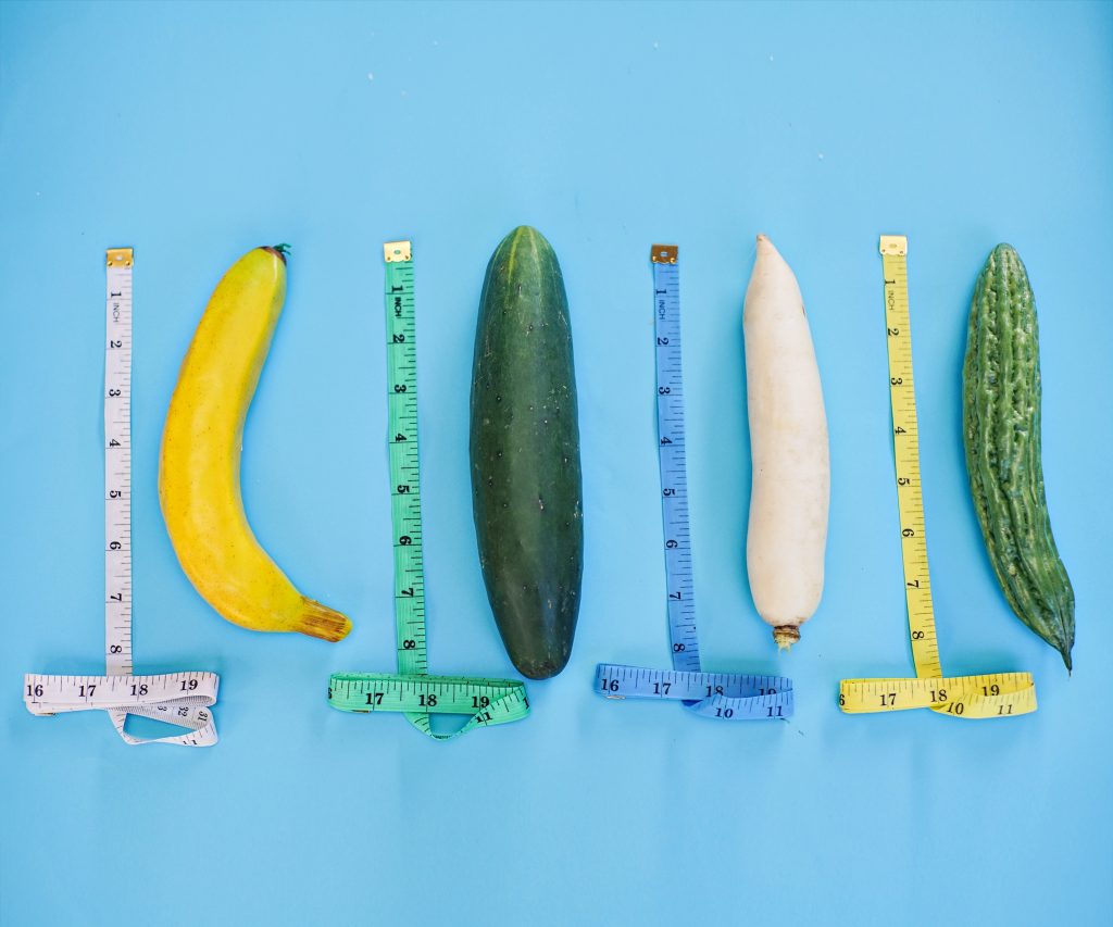 A banana, a cucumber, a carrot, and a squash with measuring tapes next to each individual vegetable.