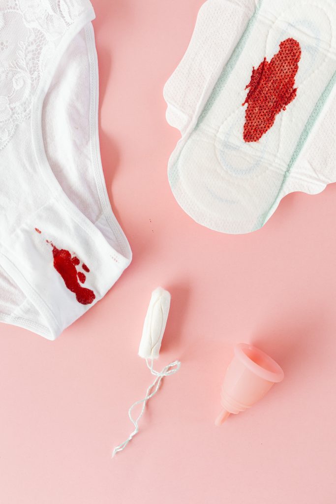 A pair of white underwear stained with blood, a pad with blood, a tampon, and a menstrual cup.