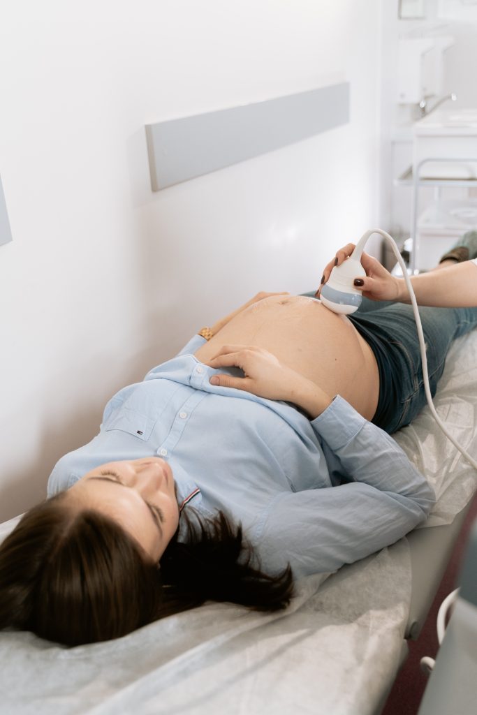 A pregnant person laying on a bed while receiving a fetal ultrasound scan.