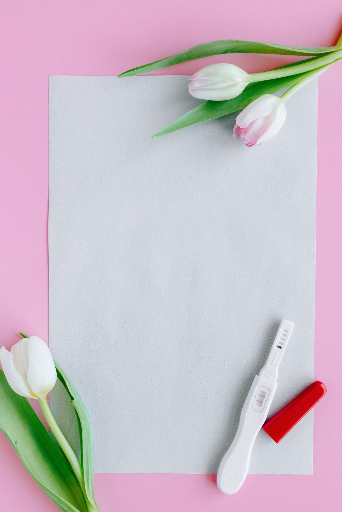 A positive pregnancy test against a white paper, with two tulips.
