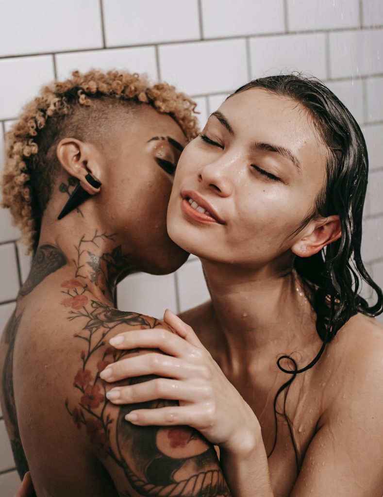 Two nude people holding each other. One person is giving the other person a kiss on the neck.
