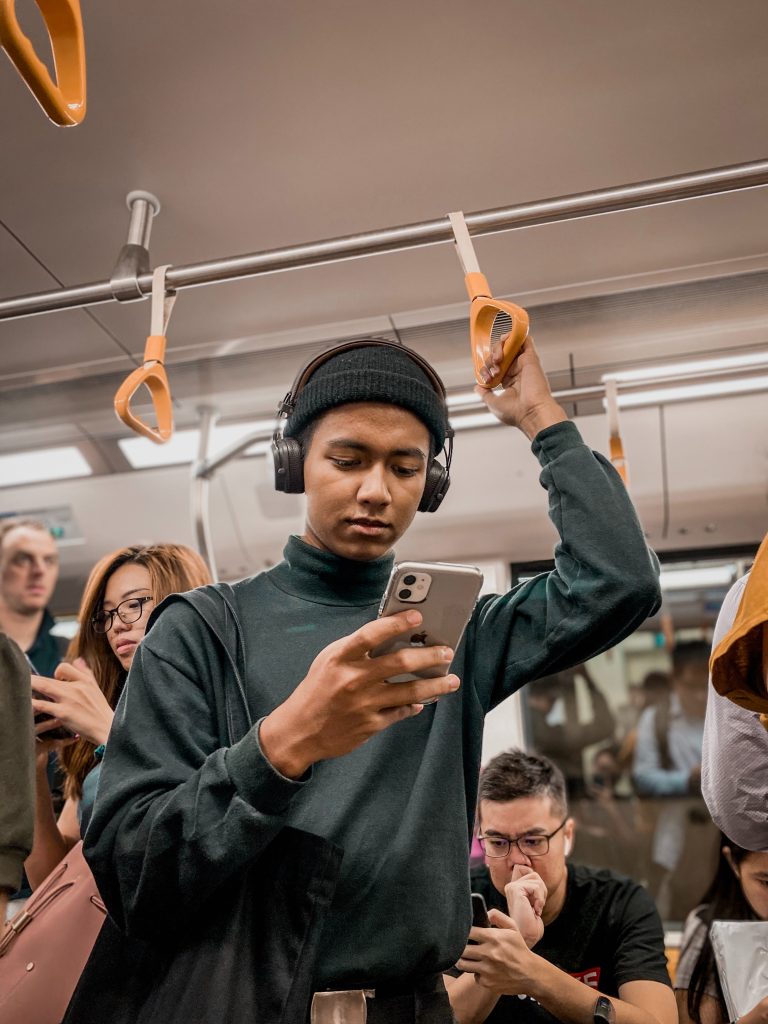 A person holding their phone in one hand while looking at it. There are multiple people surrounding the person in a bus; the individuals are also looking at their own cellphone.