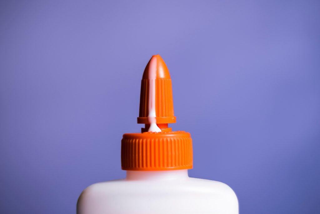 The orange top of a glue bottle leaking white milky glue.