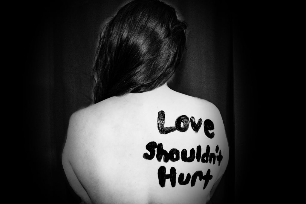 A person's bare back with "Love shouldn't hurt" painted on it.