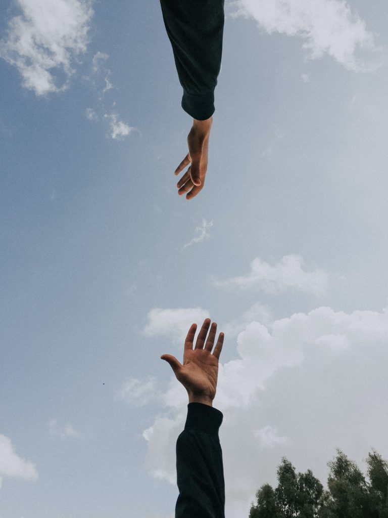Two hands reaching toward each other across a cloudy blue sky.