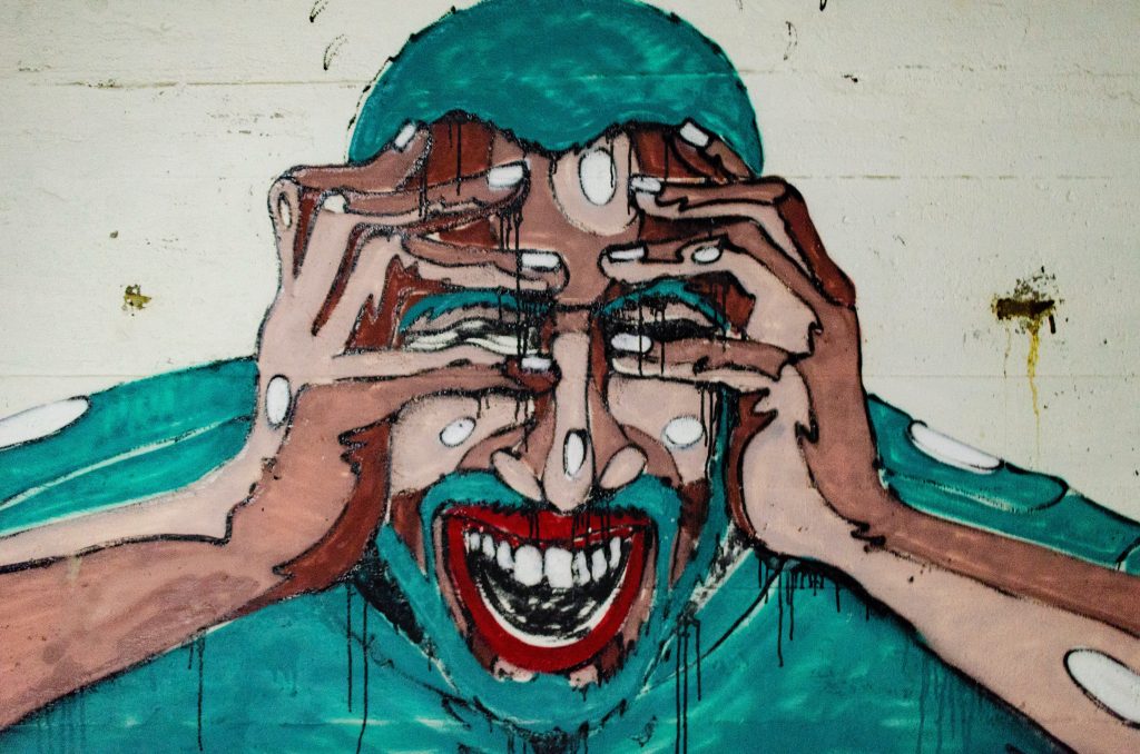 A distressed man abstractly painted in teal and red.
