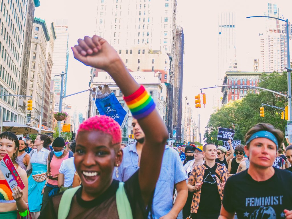 A group of people in a protest. One person has pink hair and has a rainbow bracelet.