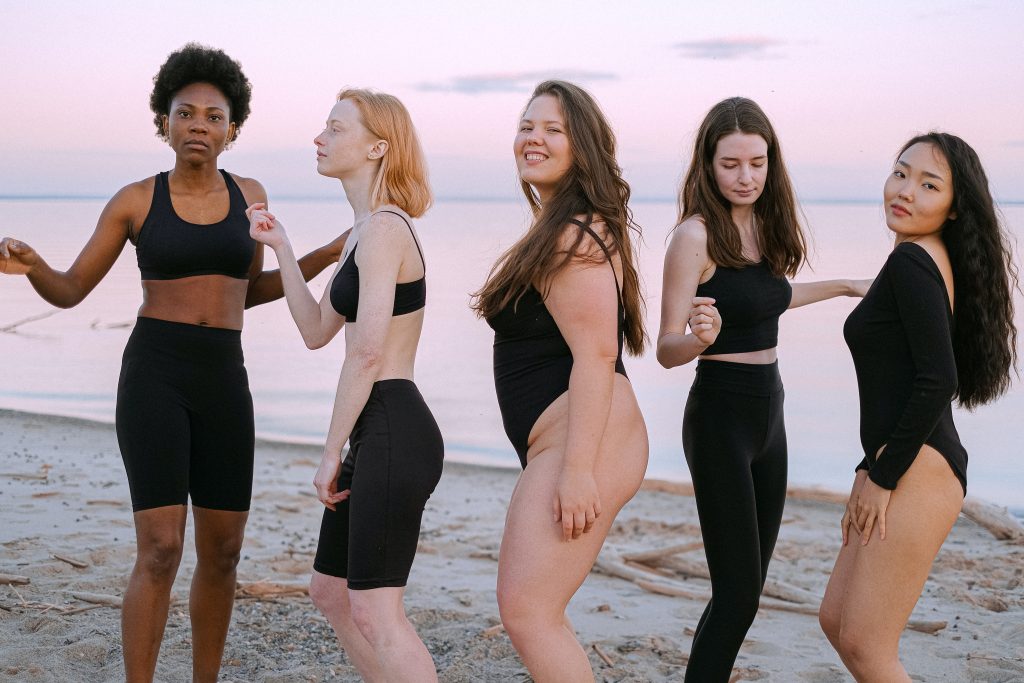 Five women in black clothing standing on sand at a beach.