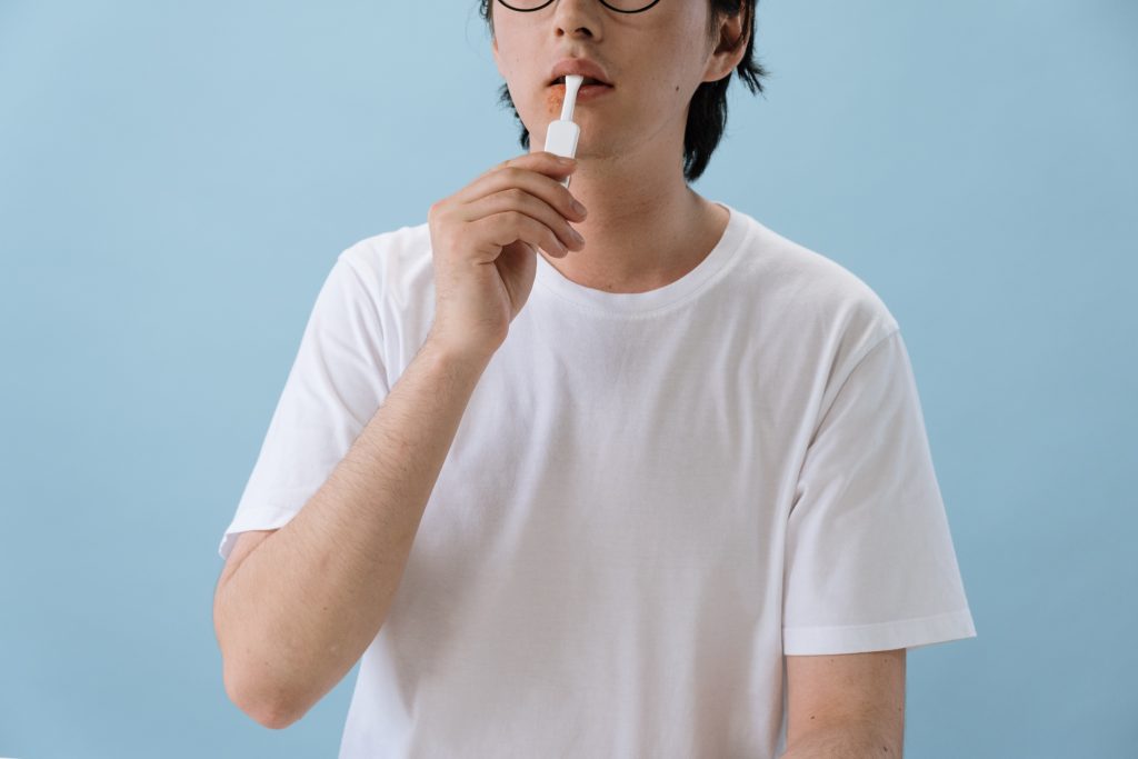 A person with cold sores on their mouth. The person is holding up a white object to their mouth.