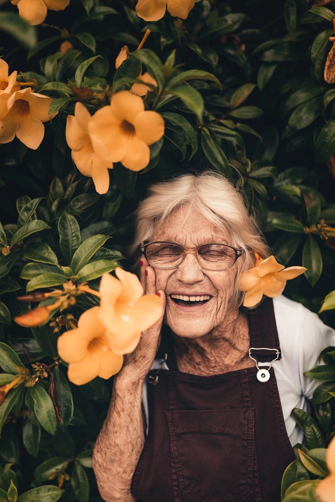 An older woman smiling next to flowers.