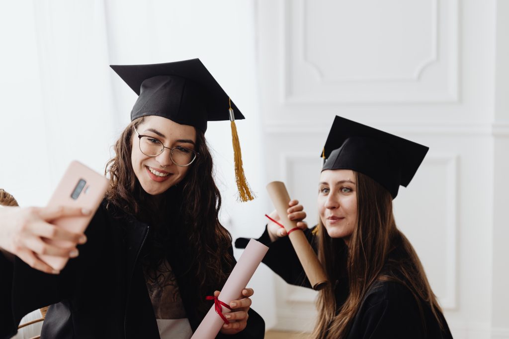 Two women in graduation caps and gowns, taking a selfie.