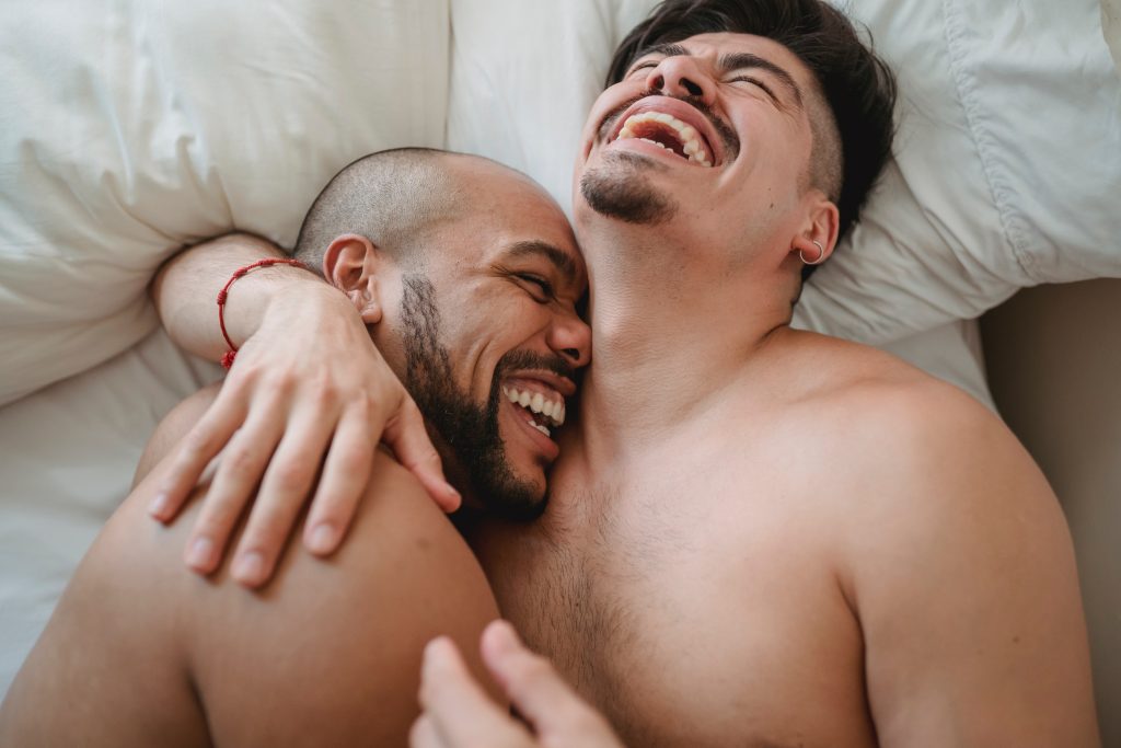 Two topless men hugging and laughing.