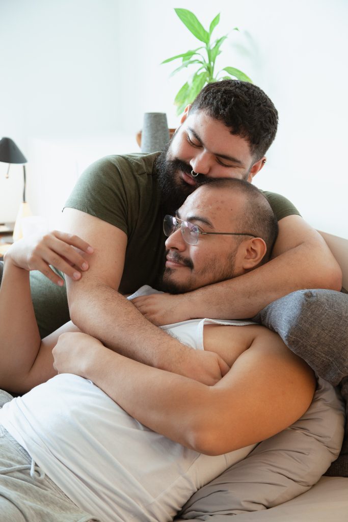 Two men closely hugging on a couch.