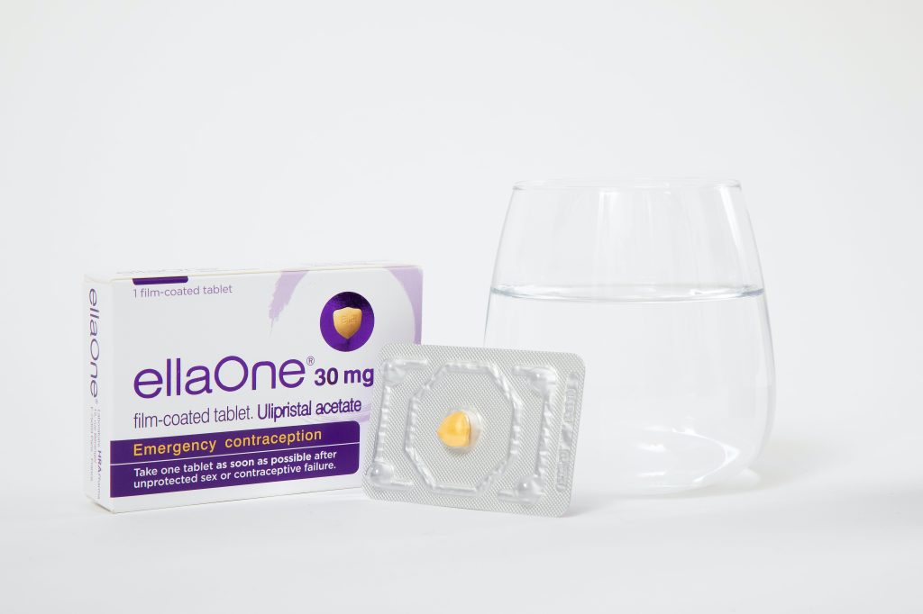 The "ellaOne" emergency contraception pill next to a glass of water.