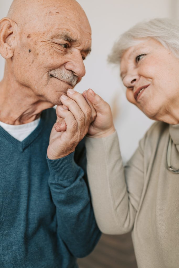 An older couple smiling at each other and holding hands.