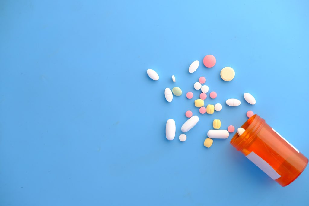 An orange pills bottle with colorful pills outside of it.