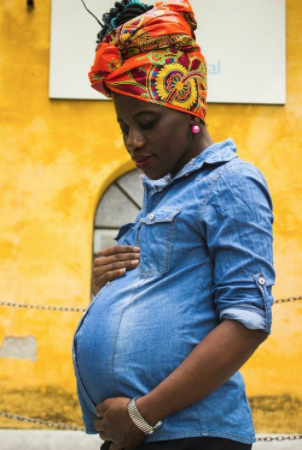 Woman clutches her pregnant belly. She is standing so her side profile is visible. 