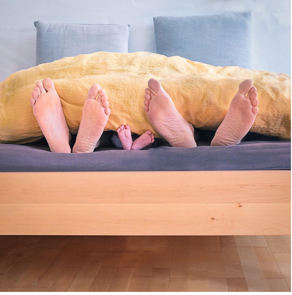 Two adults and one infant lay in bed with their feet hanging out the bottom.
