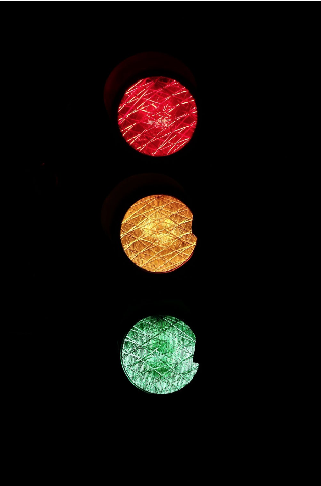 A stop light completely lit on a dark background, red on top of yellow o top of green. 