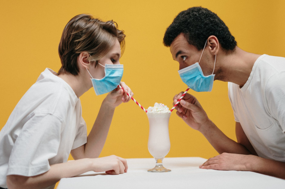 Two people sharing a drink while wearing masks.
