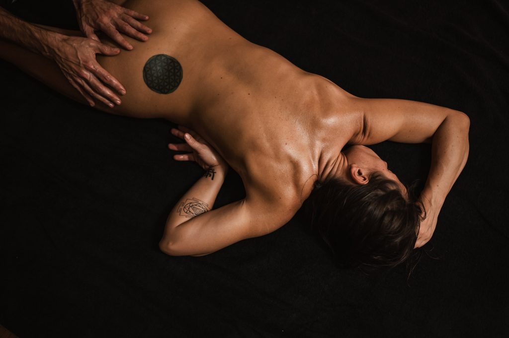 A nude person laying down while someone's hands are massaging their butt.