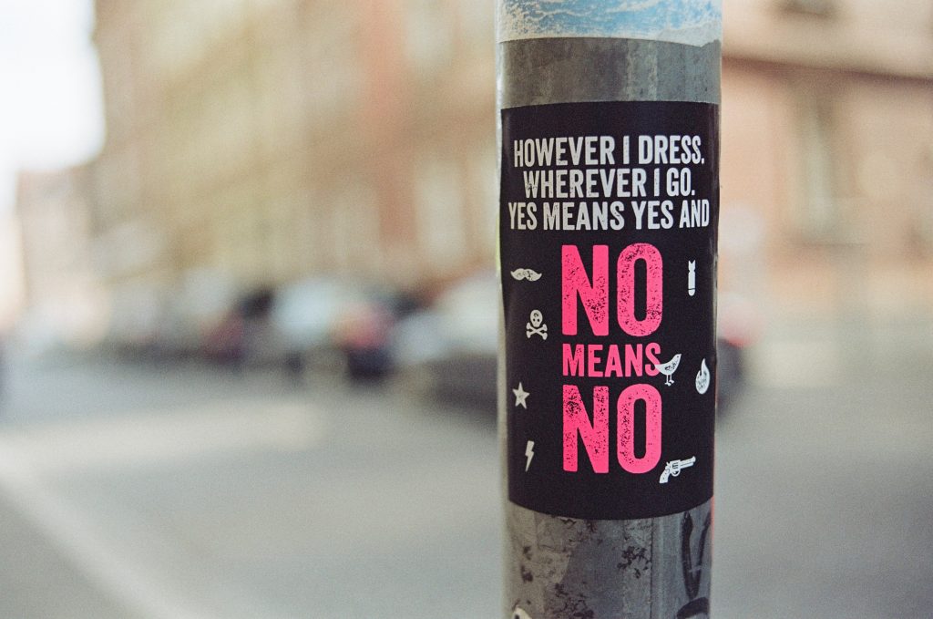 A sticker with "However I dress, wherever I go, yes means yes and no means no" stuck on a pole.