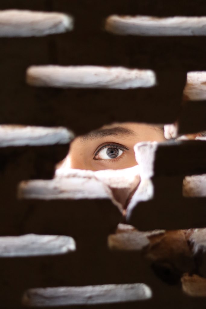 A person's eye peeping through a hole in a brick wall.