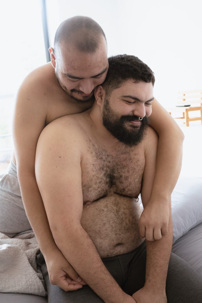Two topless men smiling and embracing each other.