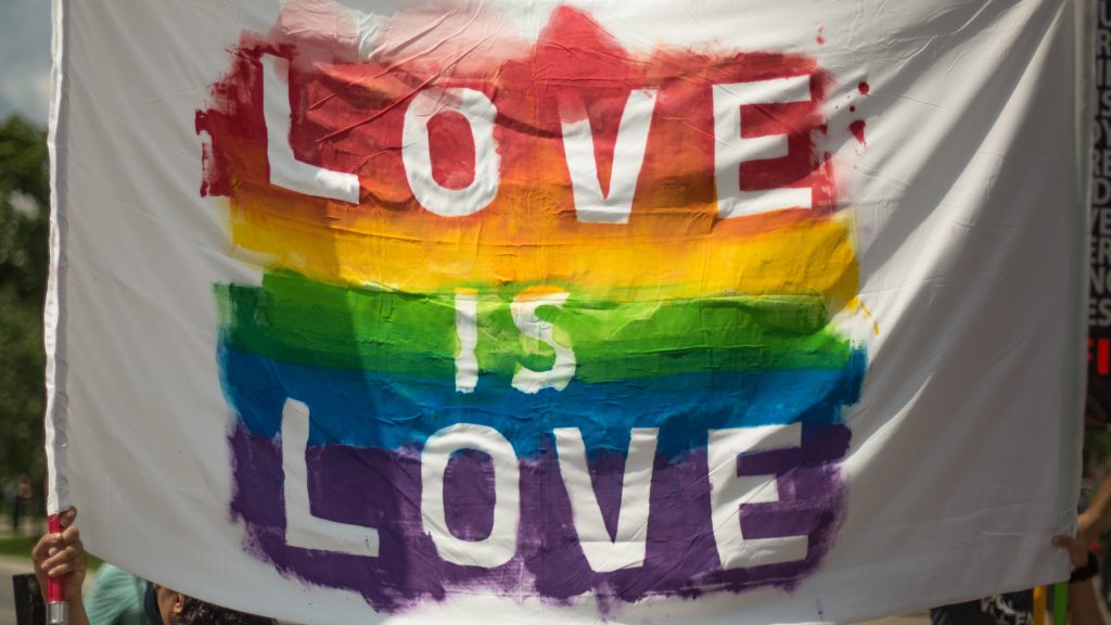 white lettering with a rainbow background on a white flag that says "Love is Love"