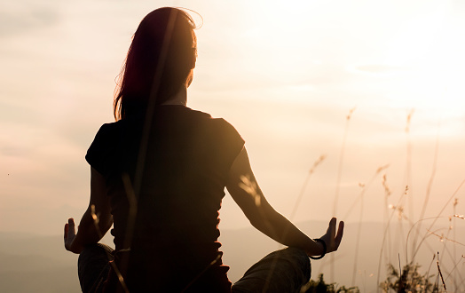 woman meditating sitting down with hands on her knees, facing the sun.