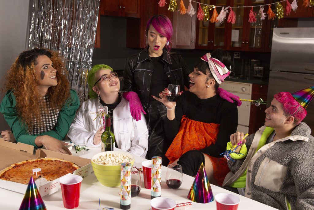 A group of people sitting around a table with food. The individuals have pink, green, and brown hair.