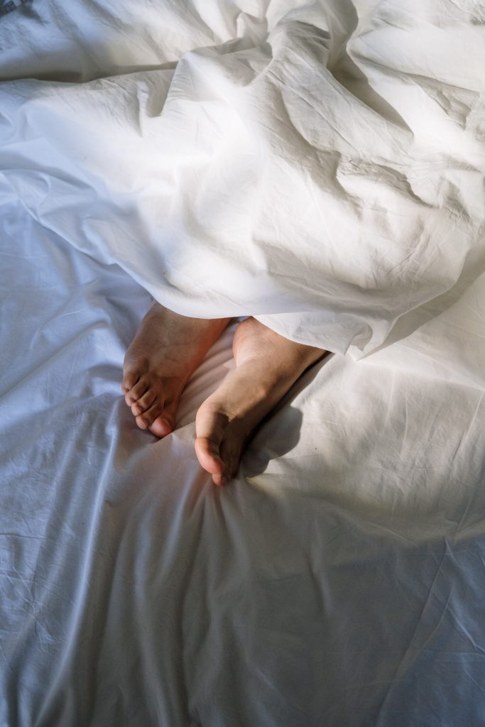 A person's feet on a bed with white sheets.
