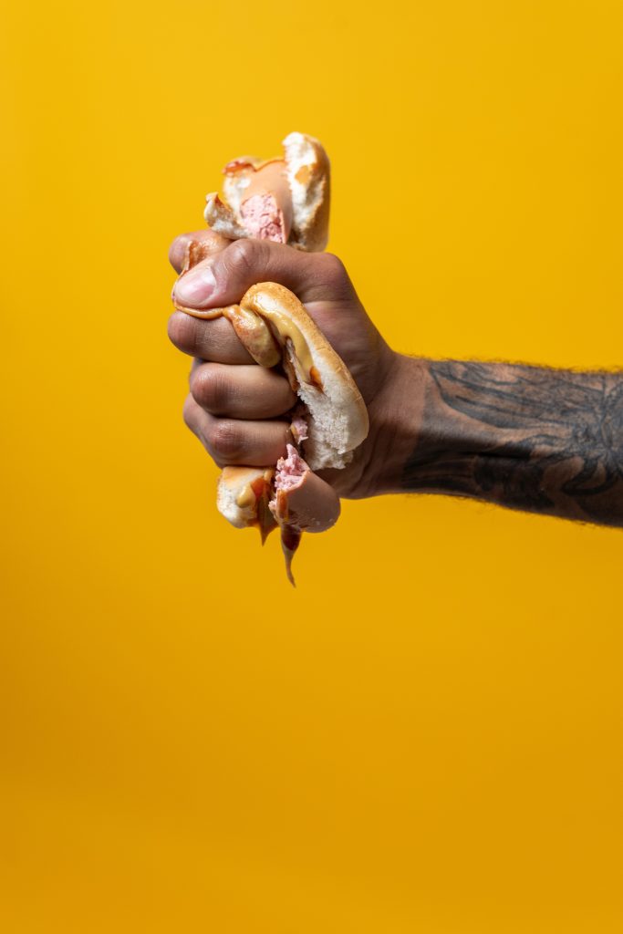 A person's hand smashing a hotdog.