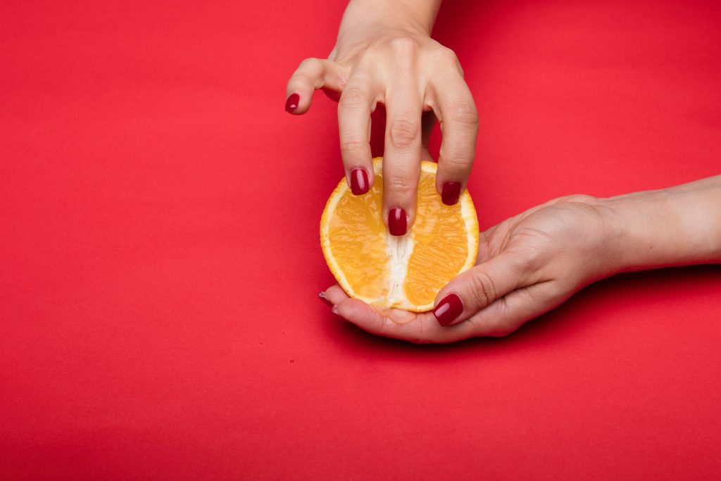 A hand fingering half an orange that resembles a vagina.