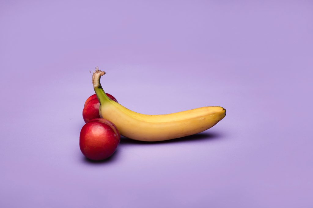 A banana with a nectarine on its left side and on its right side that resembles a penis and testicles.