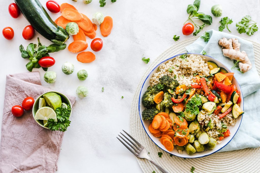 A big bowl of colorful vegetables such as zucchini, carrots, broccoli, tomatoes, limes, ginger, and quinoa.
