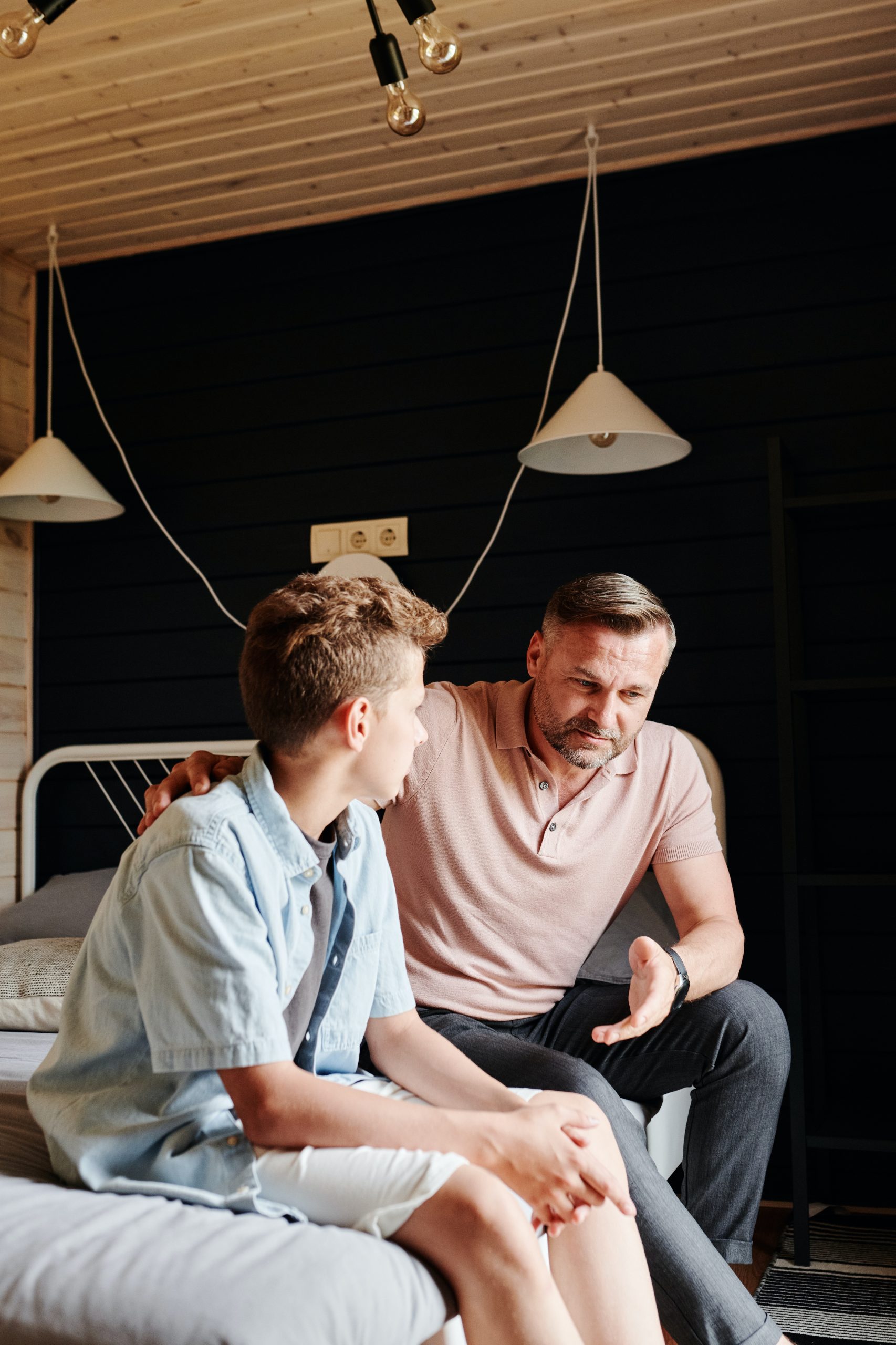 A father talking to his son while they are sitting on a bed.