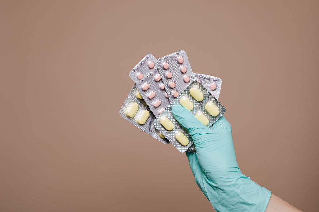 A hand with a glove holding packages of pills.