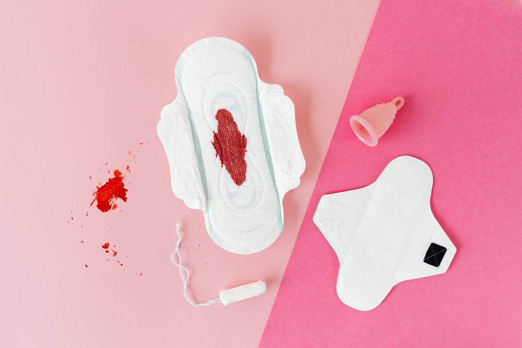 A menstrual pad with blood, a menstrual cup, a reusable pad, and a tampon.