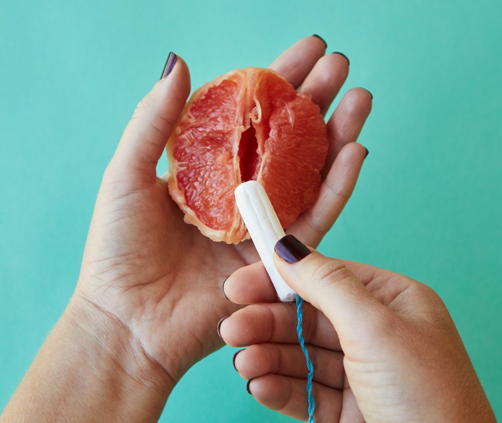 A person inserting a tampon into a grapefruit that resembles a vagina.