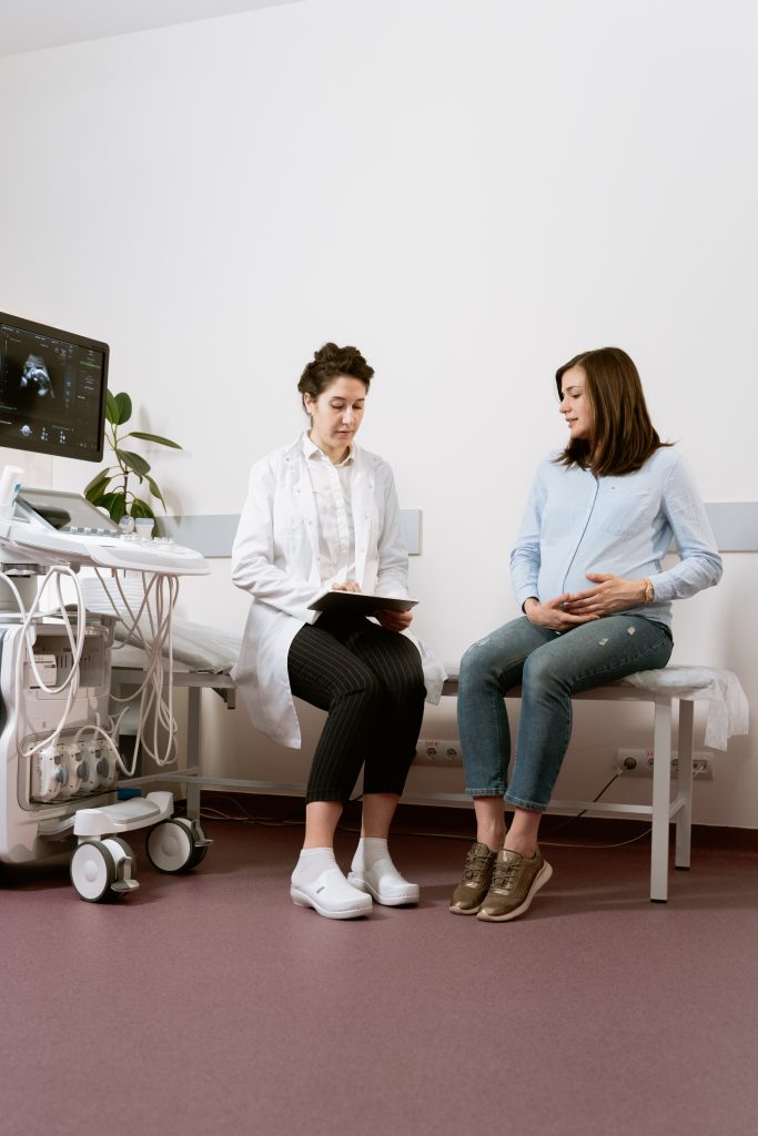 A pregnant person sitting next to a doctor in a medical room.