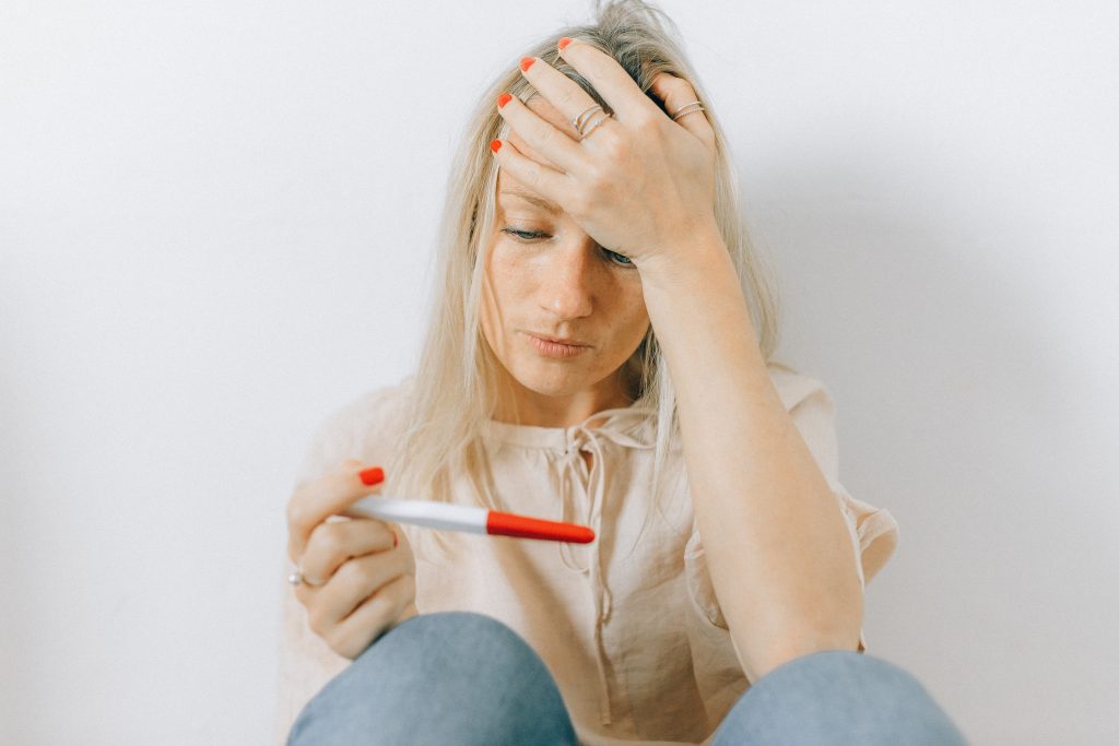 A person looking at a pregnancy test. The person has one hand on their head.