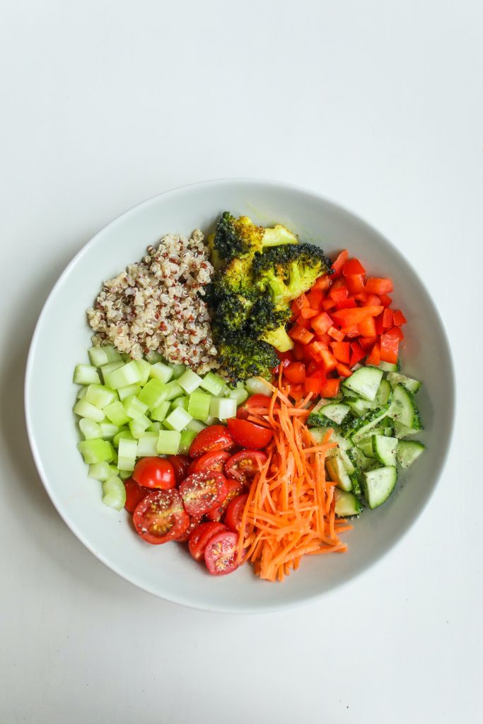 A bowl filled with broccoli, quinoa, carrots, tomatoes, and cucumbers.